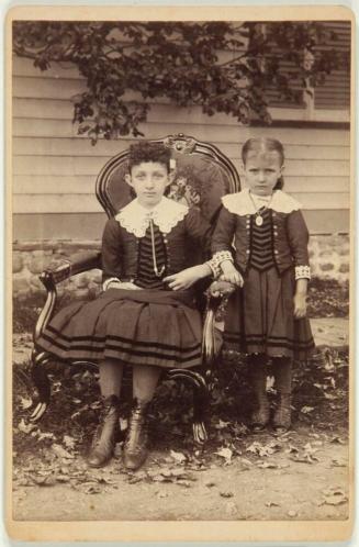 [Two Girls: One Seated in Chair, One Standing]
