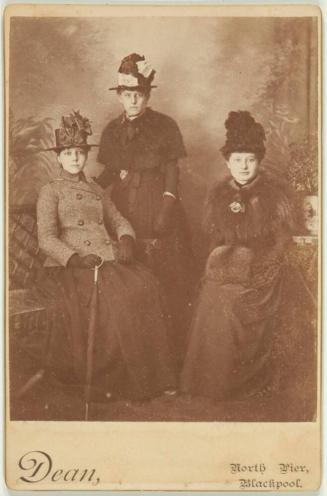 [Three Women: One Standing, Two Seated]