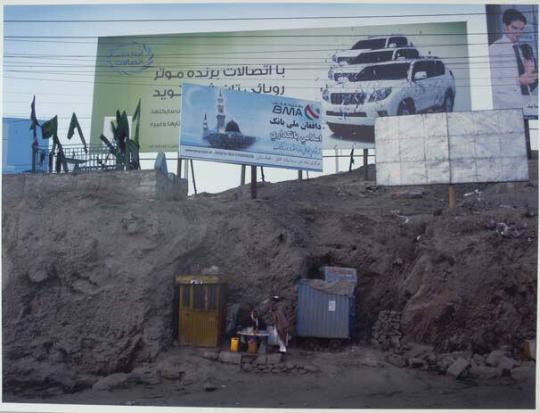 An entrepreneur creates a roadside tea stall at the busy Saraj-e Shomali traffic junction. Above him are adverts for banks; a ‘win a free car’ offer from a mobile phone company and the grave of a shahid or martyr.