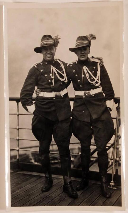 [Two men in military uniforms against rail]