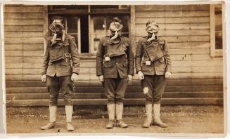 [three soldiers in uniform wearing gas masks in front of building]