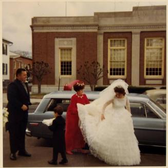 [bride getting out of car with woman in red behind her straightening dress train]