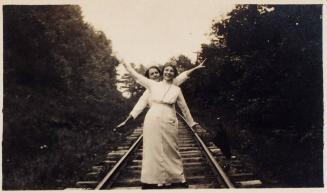 [two women in white clothing on railroad track]