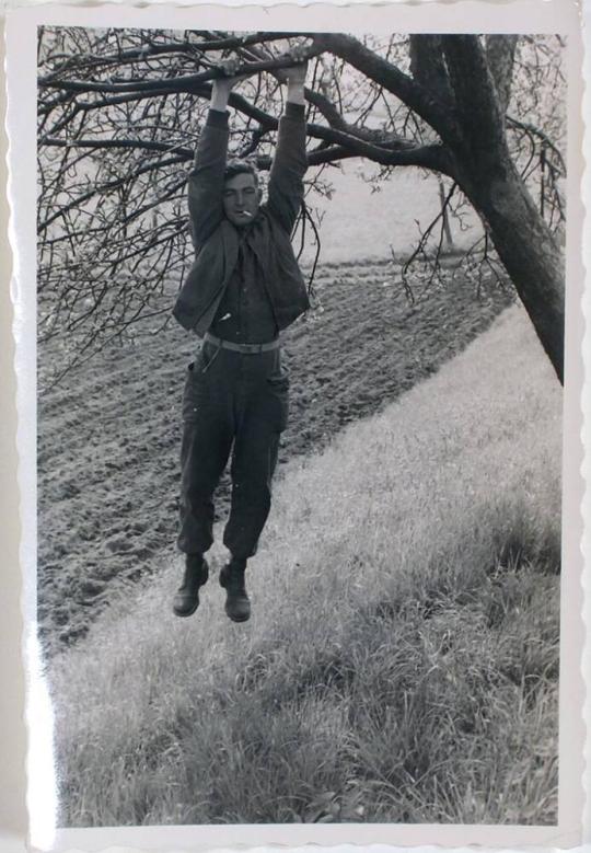 [man in military uniform hanging by two arms from tree branch]