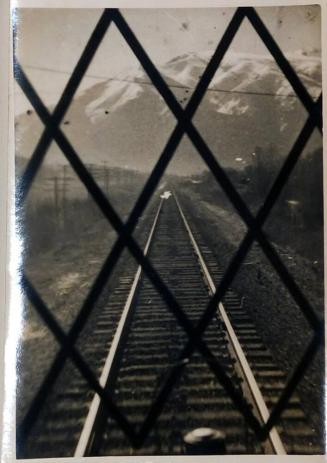[railroad tracks seen through gate with mountains in background]