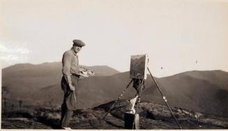 [man with hat painting on canvas on mountain]