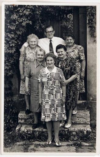 [five women in patterned dresses and one man]