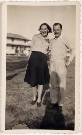 [man and woman with arms around each other on grass with building in background]