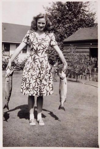 [woman holding two caught fish in yard]