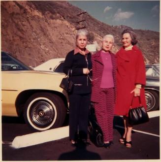 [three women standing in front of car with mountain in background]