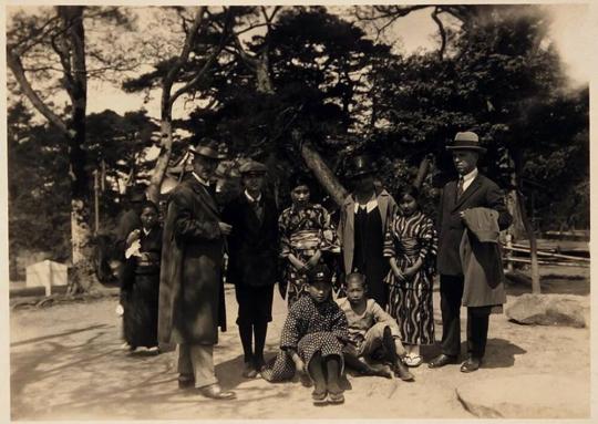 [nine people, some in kimonos, with trees in background]