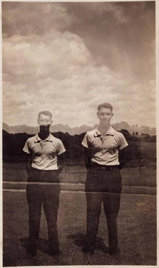 [two men dressed the same standing with arms behind backs with landscape behind]