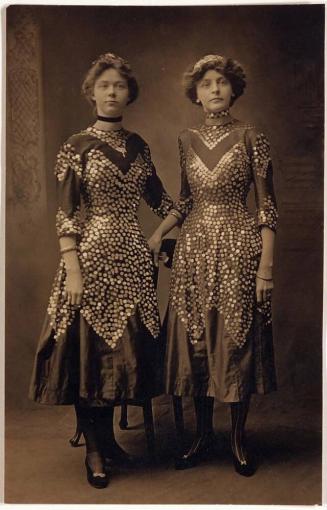[postcard- two women in the same dresses standing in front of chairs "Alma Johnson at right"]