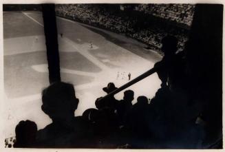 [view from the stands of a baseball game with shadows of spectators in foreground]