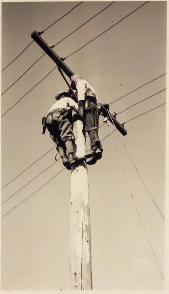 [two lineman on pole]