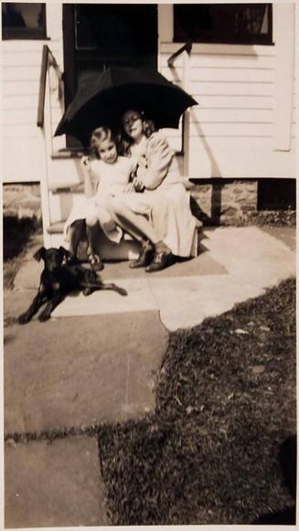[woman and girl under umbrella with dog sitting on steps of house "Sept 25 - 1943"]