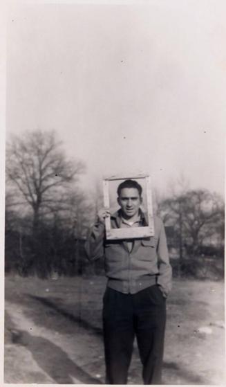 [man holding picture frame in front of face standing outdoors "April 1951 / Park."]
