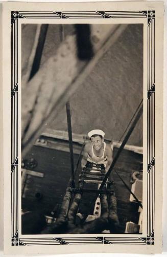 [view from above of man in sleeveless shirt, sailor hat, and glasses climbing ladder with deck of boat and water below]