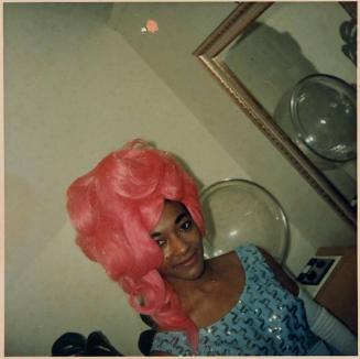 [person in pink wig with hairdryer and mirror in background]