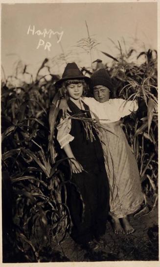 [postcard- two children dressed in costumes in corn field "Young Crossdressers? / 'Children of the Corn!'"]