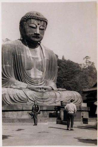 [man in front of large Buddha statue with man walking in front]