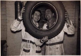[two men posing with tire in front of faces]