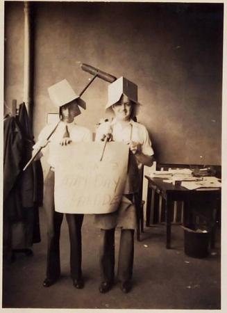 [two men wearing boxes as hats and holding push brooms holding sign "...May Day Parade"]