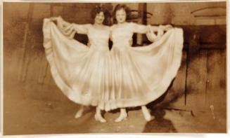[two women dressed in identical dresses each holding skirt out to side]