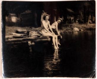 [two women sitting on edge of dock with water "Molly right is lots of fun/ Joyce on left kisses better!"]