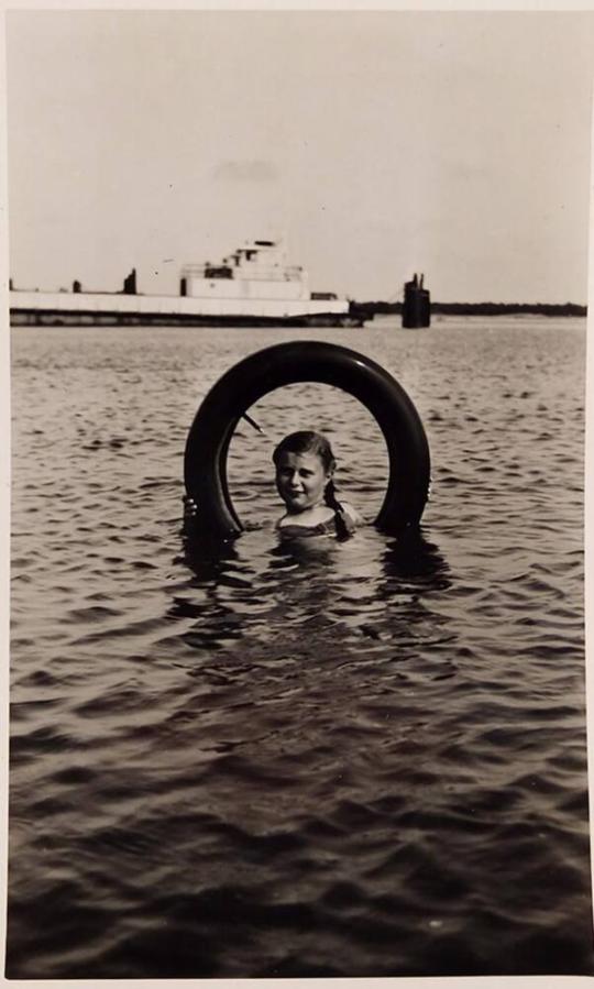 [girl in water in innertube with ship in background]