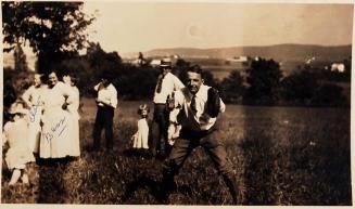 [man with catcher's glove in grassy clearing with 8 other adults and children]