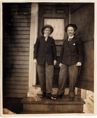 [two women in jackets standing on small porch with block of ice]