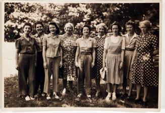 [nine women standing in a row outside in grassy area]