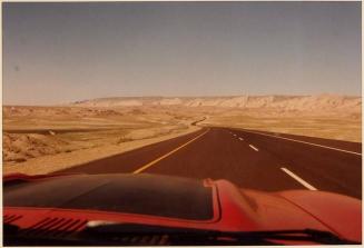 [view from inside of car looking down two lane road towards low mountains]