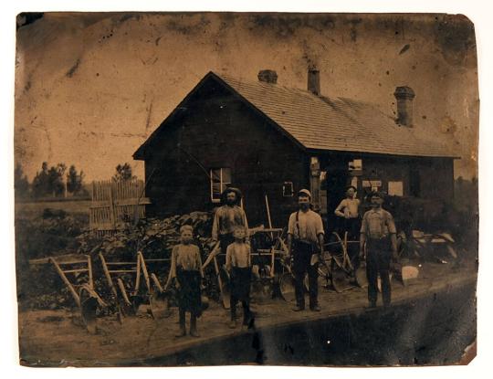 [Blacksmith and Helpers Displaying Ploughs]