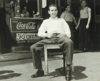 Seated Man Sunning Himself in Front of Candy Store
