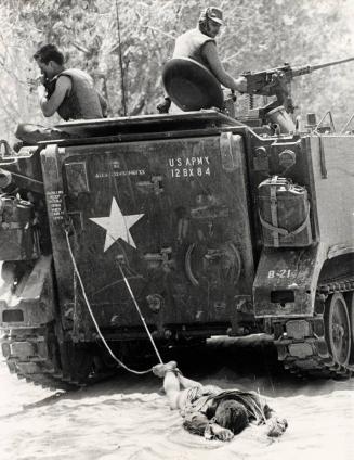 The body of a Viet Cong soldier is dragged behind an armored vehicle en route to a burial site after fierce fighting