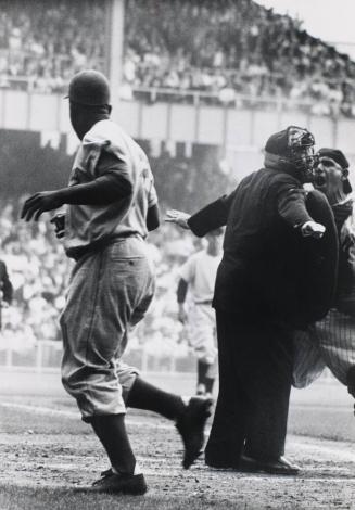 New York Yankee catcher Yogi Berra screaming in the face of the home plate umpire as he protests the official's "safe" call on Brooklyn Dodger Jackie Robinson who is walking away after a brilliant steal of home base in the 1st Game of the World Series at Yankee Stadium