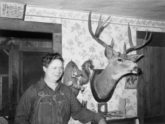 Mildred Anthony, standing by mounted animals which she killed
