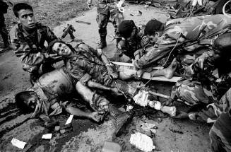 A government soldier wounded by an IED (Improvised Explosive Device) planted by FARC rebels lies alongside a dead friend while medics attach splints to his shattered legs, Paujil, Caqueta, Colombia.