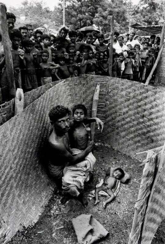 The dead body compound of a refugee camp: A man places his nine-year-old son next to the body of a one-year-old boy