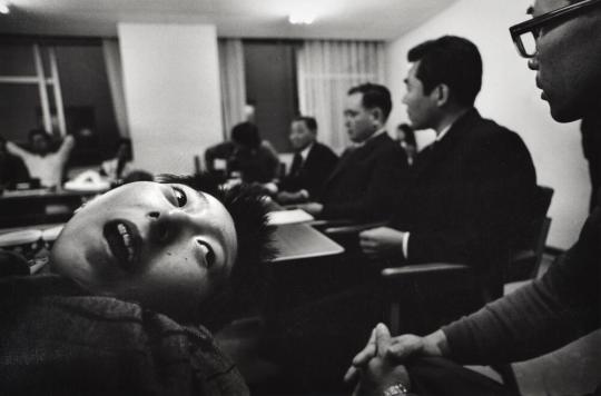 Tomoko Uemura, a victim of mercury poisoning, is taken to the Central Pollution Board, during the Victims of the Minamata Disease versus the Chisso Chemical Plant trial. The patients demanded that the members of the Board look, touch, and hold her.