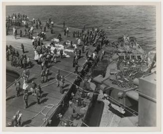 Survivors, including some injured, are photographed on the flight deck of the FRANKLIN as they await transferral to the SANTA FE, secured alongside the carrier