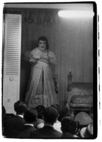 Female impersonator on stage in a ruffled gown showing her breast, Hubert’s Museum, N.Y.C.