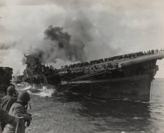 The USS Franklin, blasted by a Japanese dive-bomber in March 1945, lists sharply to starboard as the USS Santa Fe approaches.