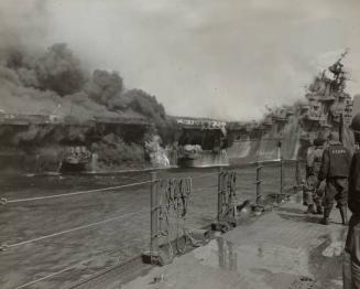 Seething banks of smoke envelop the stern of the FRANKLIN as flames race through the interior of the ship.  Men of the Cruiser SANTA FE watch in fascinated horror as they await the opportunity to lend a hand. Burning gasoline escapes out of the side of the ship, while a group of survivors clambore down a cargo net at the far left.