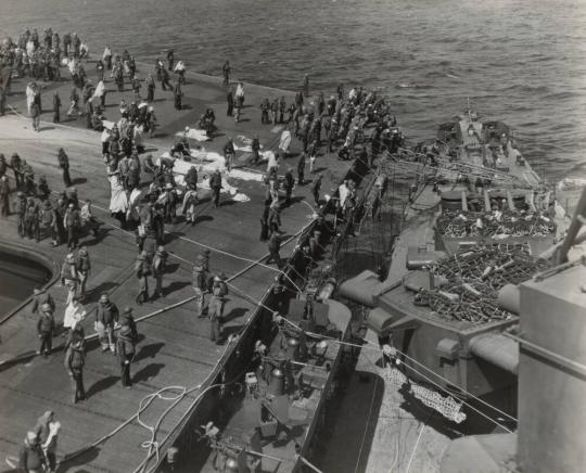 Survivors, including some injured, are photographed on the flight deck of the FRANKLIN as they await transferral to the SANTA FE, secured alongside the carrier