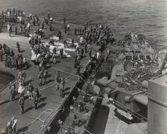 Survivors, including some injured, are photographed on the flight deck of the FRANKLIN as they await transferral to the SANTA FE, secured alongside the carrier