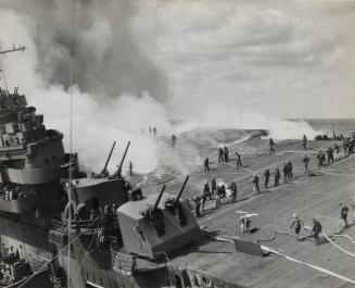 The list of the FRANKLIN affords an unusually clear vision of the extent of the havoc on the flight deck.  Tongues of flames run along the wooden surface as crewmen converge on the endangered area with firehose.  Despite the appalling shock of the explosion, the undamaged guns went into action when the japanese loosed a follow-up aerial attack, and succeeded in driving the few away without sustaining further hits.