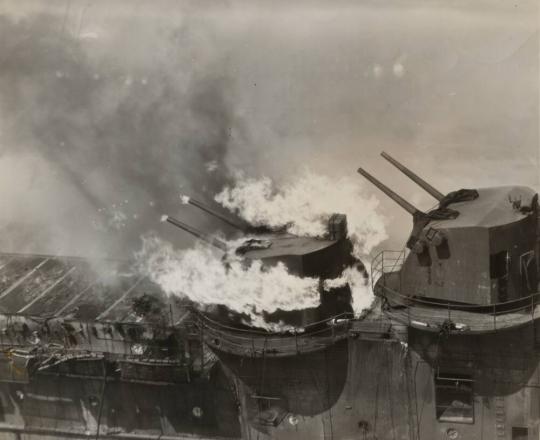 A crown of flame mantles one of the five-inch turrets on the FRANKLIN, with jets of fire flickering out of the muzzles of the twin rifles.  Crewmen aboard the cruiser SANTA FE extinguished the blaze by playing streams of water through the open hatch.